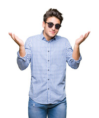 Young handsome man wearing sunglasses over isolated background clueless and confused expression...
