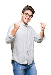 Fototapeta premium Young handsome man wearing glasses over isolated background very happy and excited doing winner gesture with arms raised, smiling and screaming for success. Celebration concept.