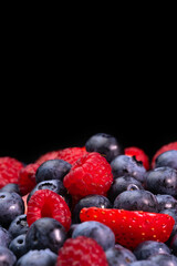 Colorful berries close-up on a black background, front view, macro photography. Blueberries, raspberries, strawberries. Concept of healthy nutrition. Vertical photo