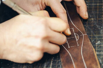 Close up of a shoemaker or artisan worker hands. Leather craft tools on old wood table.