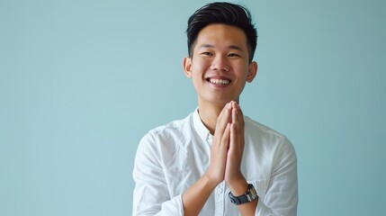 Young, attractive, smiling man from Southeast Asia clapping hands against a blue backdrop - obrazy, fototapety, plakaty