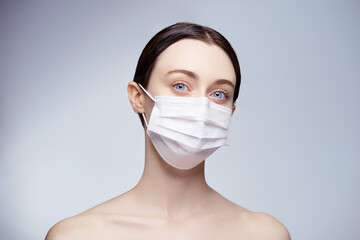 Portrait of a young beautiful woman in a medical mask on a white grey background.