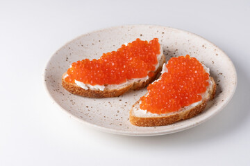 Two sandwiches with red caviar on a plate. A delicious appetizer of trout caviar on a slice of bread with cream cheese. Salted salmon caviar for fish delicacy concept