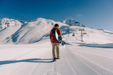 snowboarder holding snowboard walking along ski slope at  resort prepared by snowcat