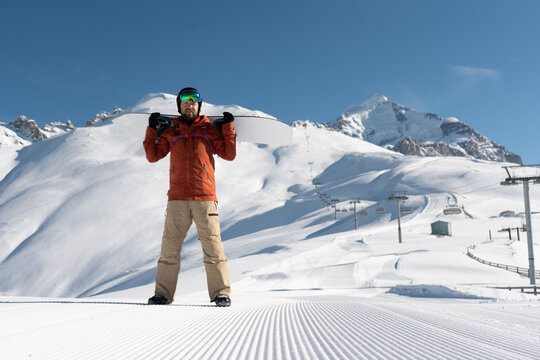 snowboarder holding snowboard standing and posing along ski slope at  resort prepared by snowcat