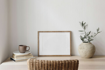 Empty horizontal picture frame mockup. Wooden table, desk with cup of coffee, blurred rattan chair....