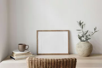Foto auf Acrylglas Empty horizontal picture frame mockup. Wooden table, desk with cup of coffee, blurred rattan chair. Vase with olive tree branches, old books. Mediterranean interior, home. White wall background. © tabitazn