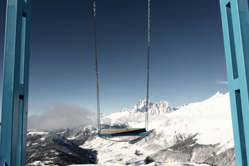 Empty swing against backdrop of winter mountain peaks, no people, sunny day