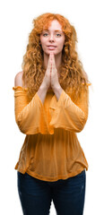 Young redhead woman praying with hands together asking for forgiveness smiling confident.