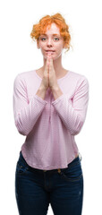 Young redhead woman praying with hands together asking for forgiveness smiling confident.