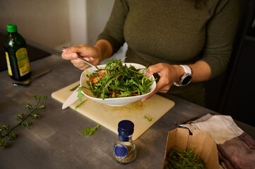 Close-up woman hands holding a white bowl of fresh healthy salad with greens, arugula and tomatoes.