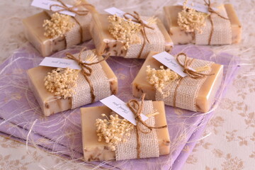 Fototapeta na wymiar Wedding favours lavender natural artisan soap, thank you handmade gifts for guests with white jute decoration and dry flowers on purple background, rustic countru style party decor