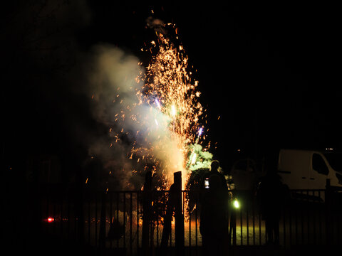 On New Year's Eve, people watch the cllorful and bright fireworks at night in a outdoor parking lot.