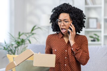 Surprised african american woman with curly hair talking on phone, unhappy with delivery