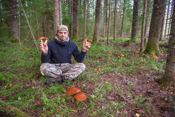 A European man holds mushrooms in his hands. There are many nribs growing between the trees.