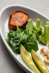 Healthy bowl with baked sweet potato, avacado, spinach, broccoli and shrimp close-up