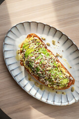 Healthy avocado toast for breakfast or lunch with whole grain bread and assorted seeds on a wooden table. Holistic nutrition concept