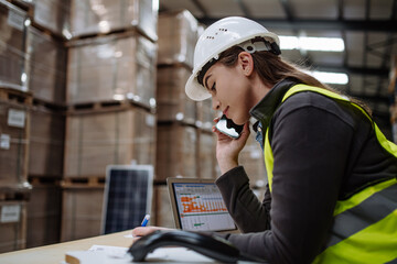 Warehouse worker checking delivery, stock in warehouse on computer, pc, while phone calling with...