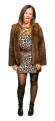 Beautiful middle age elegant woman wearing mink coat sticking tongue out happy with funny expression. Emotion concept.