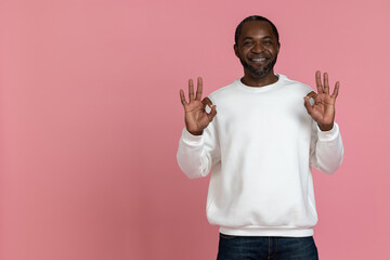 Cheerful black man wearing white sweatshirt showing approved gesture