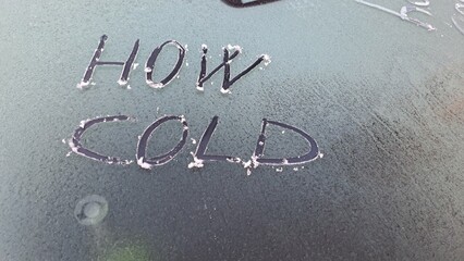 How cold written on a snow covered windshield car.