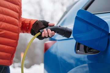Close up of charging electric car during cold snowy day, Charging and driving electric vehicles during winter season.