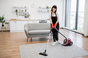 Professional female cleaner in apron actively cleans modern apartment and looking at camera....