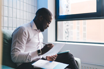 Concentrated black man writing notes in documents in office