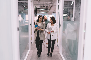 Cheerful diverse coworkers walking in contemporary office hallway