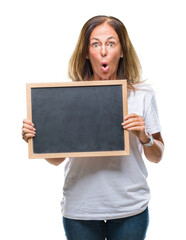 Middle age hispanic woman holding blackboard over isolated background scared in shock with a surprise face, afraid and excited with fear expression