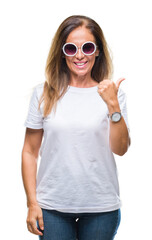 Middle age hispanic woman wearing fashion sunglasses over isolated background doing happy thumbs up gesture with hand. Approving expression looking at the camera with showing success.