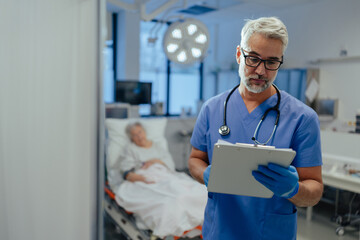 Portrait of handsome male doctor, patient in hospital bed behind. ER doctor examining senior patient, reading her medical test, lab results in clipboard. - obrazy, fototapety, plakaty