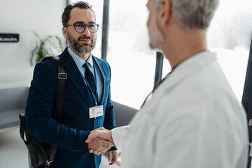 Pharmaceutical sales representative shaking hands with doctor in medical building. Doctor greeting...