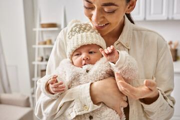 attractive caring mother in comfortable homewear holding warmly her baby boy, modern parenting