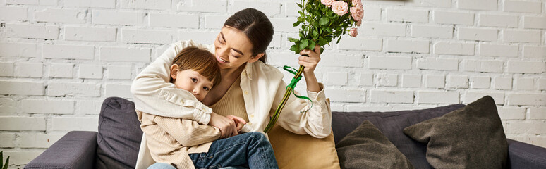 beautiful mother posing on sofa with her cute toddler son with flower bouquet, Mothers day, banner