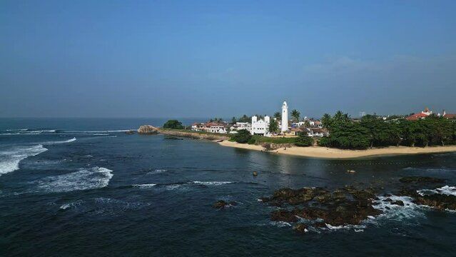 Drone footage shows Galle Fort, its lighthouse, coastline, highlighting Sri Lankas heritage, architecture, tourism potential, natural beauty in serene tropical setting suitable for diverse media use.