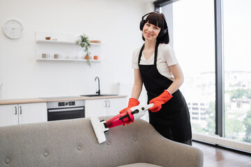 Portrait of professional young cleaner vacuuming sofa with portable cordless vacuum cleaner,...