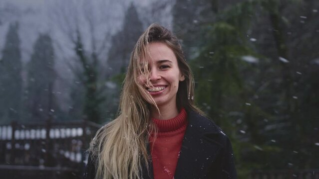 The girl in braces. Portrait of a woman in a park in winter. The female smiles, enjoys the snowfall, shows teeth with brackets. It stands against the background of Christmas trees.