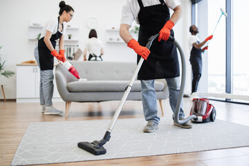 Cropped view of professional cleaner from cleaning service vacuums carpet using wireless vacuum...