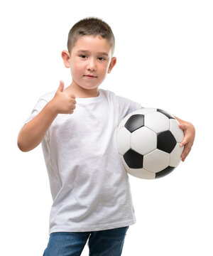 Dark haired little child playing with soccer ball happy with big smile doing ok sign, thumb up with fingers, excellent sign