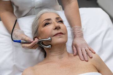 Mature woman having micro current therapy at beauty clinic