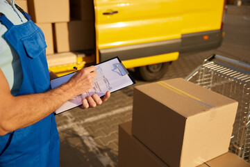 Professional male courier filling out delivery form on postal parcels