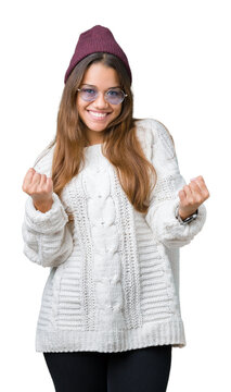 Young beautiful brunette hipster woman wearing sunglasses over isolated background very happy and excited doing winner gesture with arms raised, smiling and screaming for success. Celebration concept.