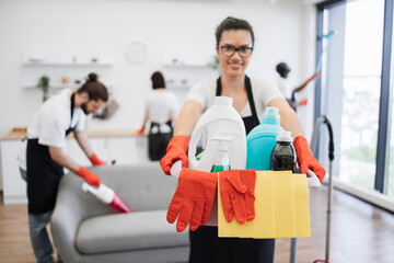 Focus on bucket for washing with detergents in hands of young African American woman professional cleaning worker bright kitchen studio background, copy space.