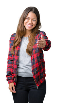 Young beautiful brunette woman wearing a jacket over isolated background smiling friendly offering handshake as greeting and welcoming. Successful business.
