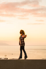 People and freedom lifestyle concept with happy free woman walking balanced with ocean and sunset in background - travel and summer holiday vacation female enjoying leisure alone