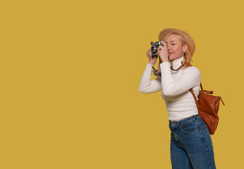 a woman in jeans, a white shirt, and  hat carrying a suitcase and taking photos by vintage camera on a yellow background. Happy people going on holiday, vacation