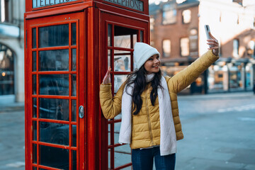 Outdoor portrait of woman using camera   against red phonebox in English city