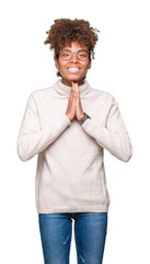 Beautiful young african american woman wearing glasses over isolated background praying with hands together asking for forgiveness smiling confident.