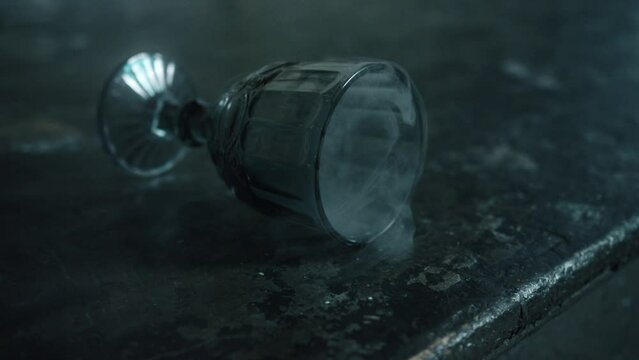 White smoke flies out of a glass goblet lying on the concrete floor. Gothic glass. Dark gloomy mysterious atmosphere. Cinematic concept of metaphor and fashion. Close up, 4K